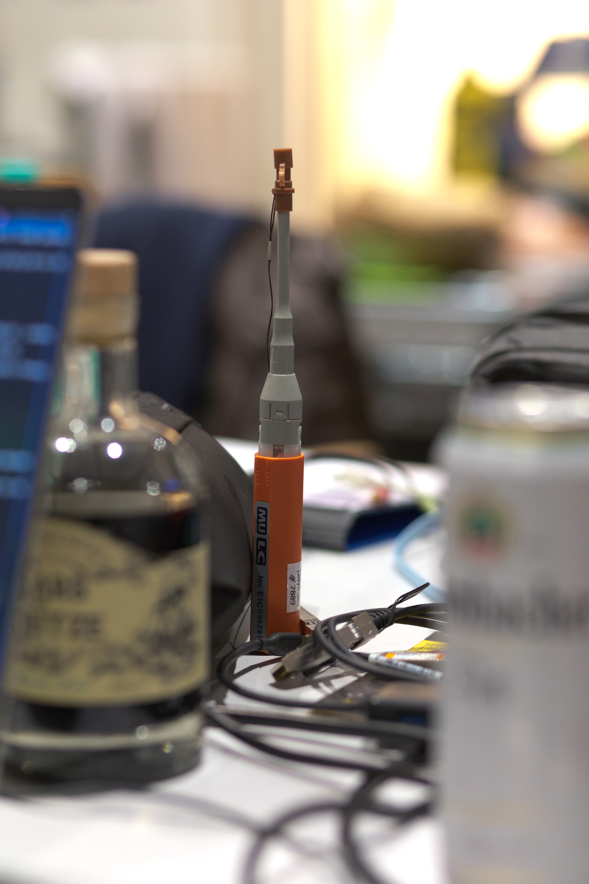 A cleaner for LC fiber optics connectors stands upright on a table. It's surrounded by stuff that's out of focus.