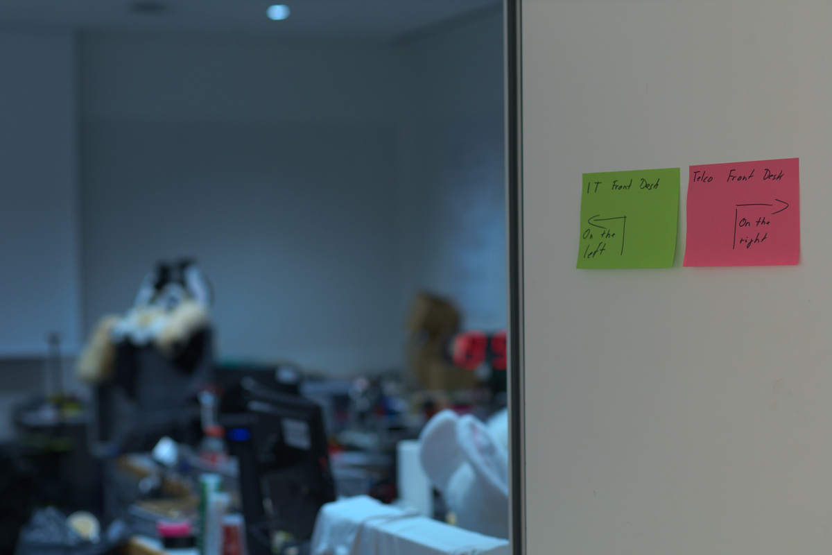 Two post-its are stuck on a door. They tell visitors that the IT front desk is on the left and the Telco front desk is on the right side.